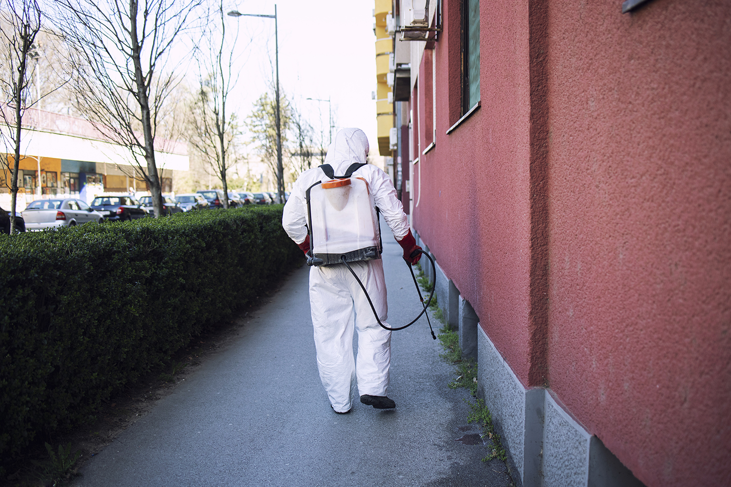 Unrecognizable worker in chemical protection suit spraying disinfectant on public surfaces.